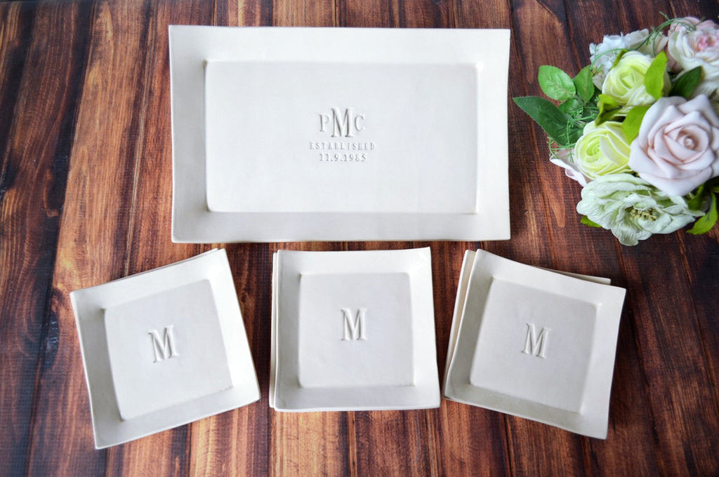 A white rectangular wedding platter with a set of 6 appetizer plates, all personalized with the initial 'M'. The platter and plates are displayed on a wooden surface with a floral decoration in the background.