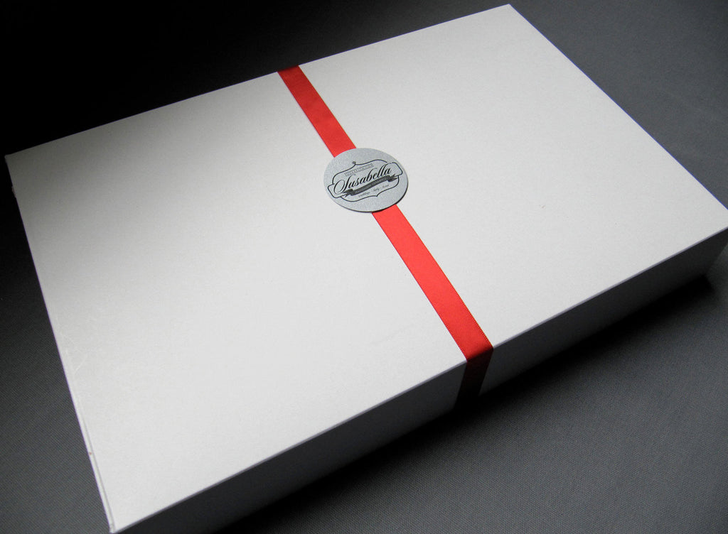 White box with a red ribbon and a silver label on a dark surface