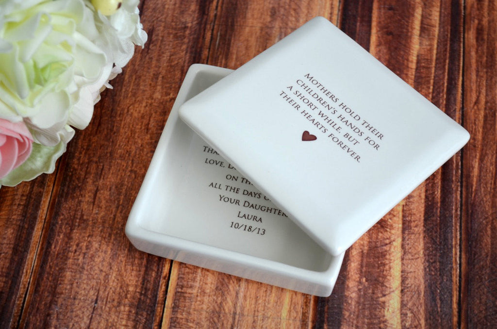 White ceramic heart-shaped object with engraved text on a wooden surface with flowers.