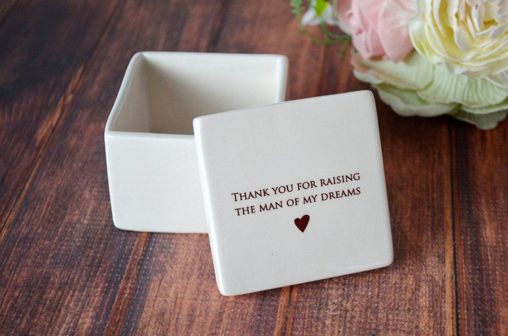 White jewelry box with engraved message on a wooden surface with flowers in the background