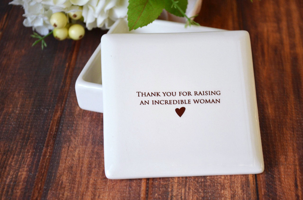 White ceramic coaster with 'Thank you for raising an incredible woman' text on a wooden surface.