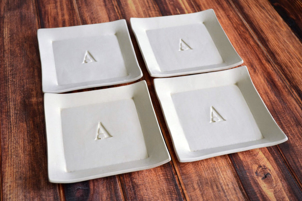 Four square ceramic dishes with letter 'A' on a wooden surface