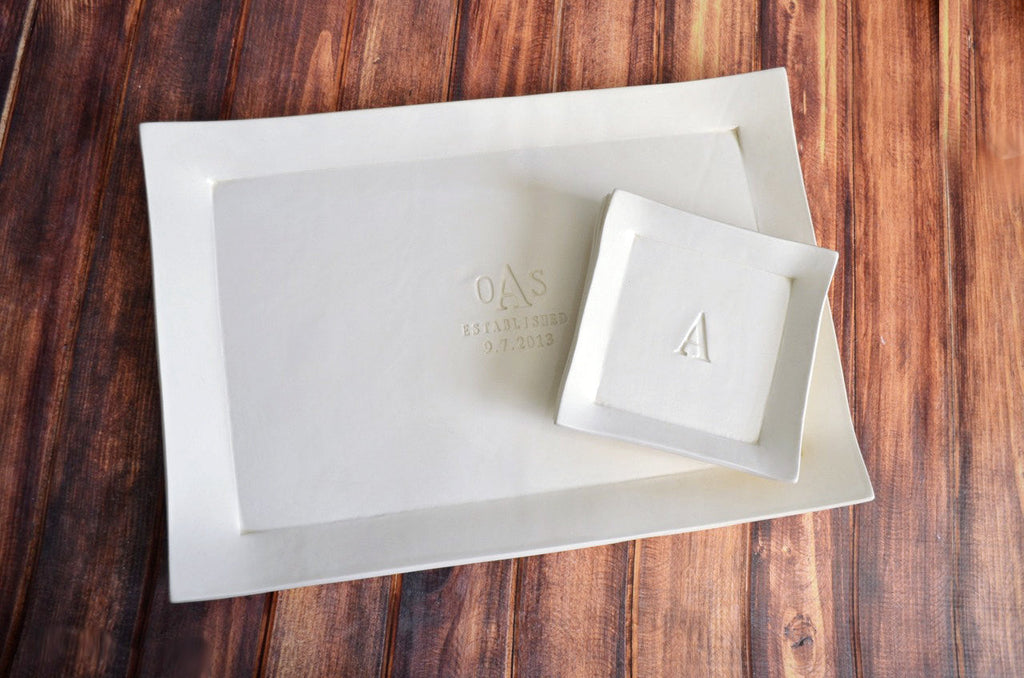 Two white ceramic trays with engraved initials on a wooden surface
