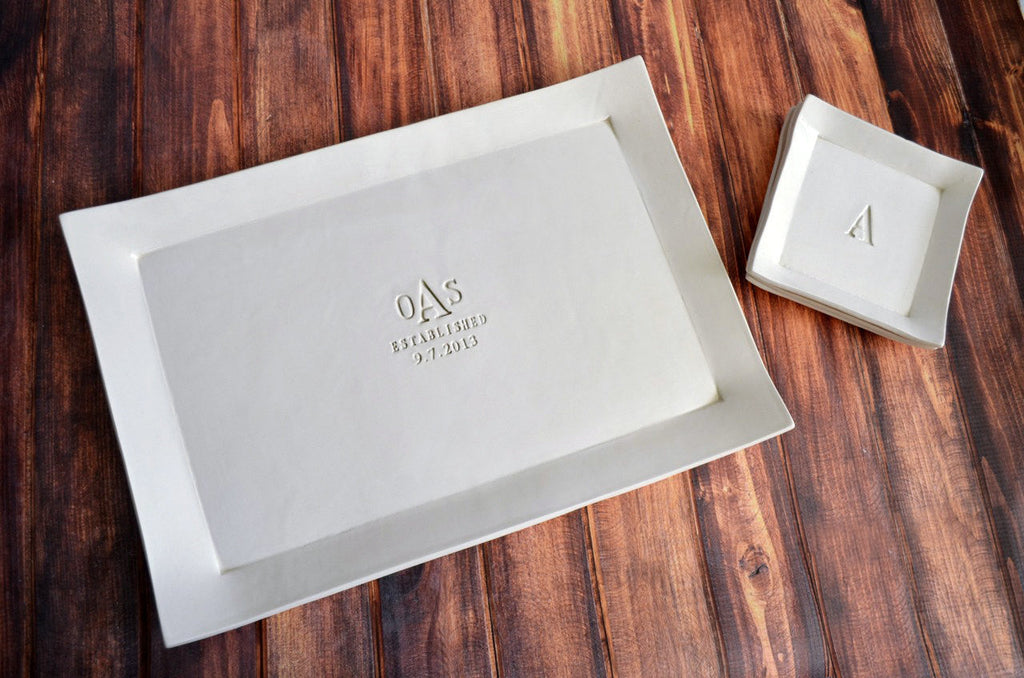 White ceramic platter and bowl with engraved initials on a wooden surface