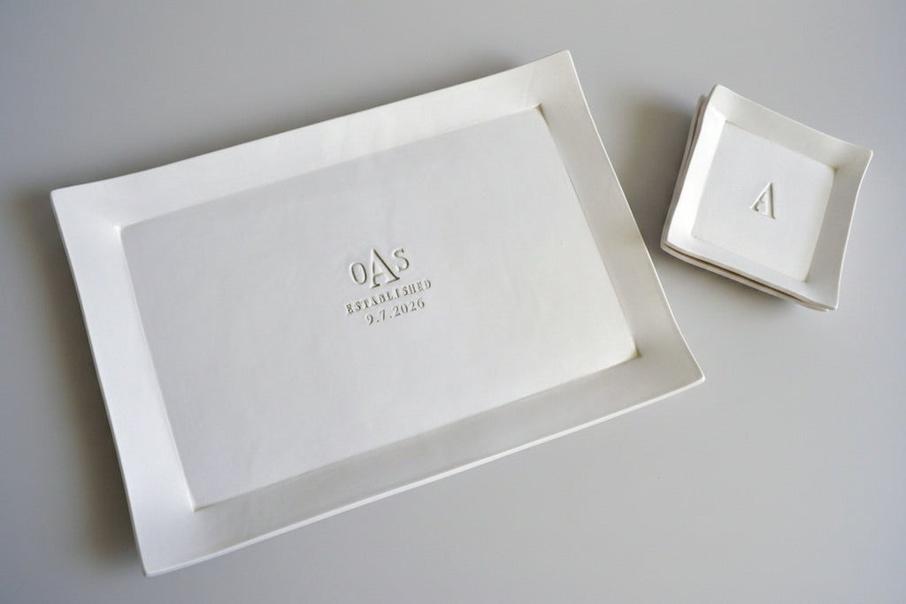 White ceramic platter and bowl with engraved initials on a wooden surface