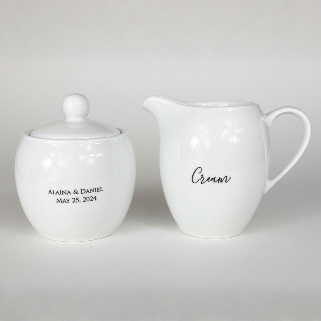 White ceramic sugar bowl and cream pitcher with personalized text on a light gray background