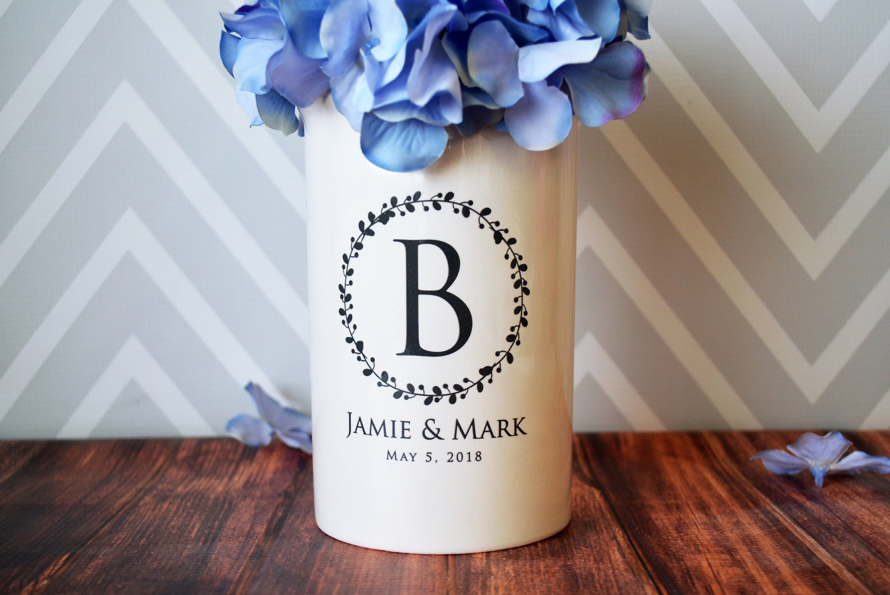 A white ceramic vase with a wreath design and a large initial in the center, personalized with the names 'Jamie and Mark' and a date 'May 9, 2019'.
