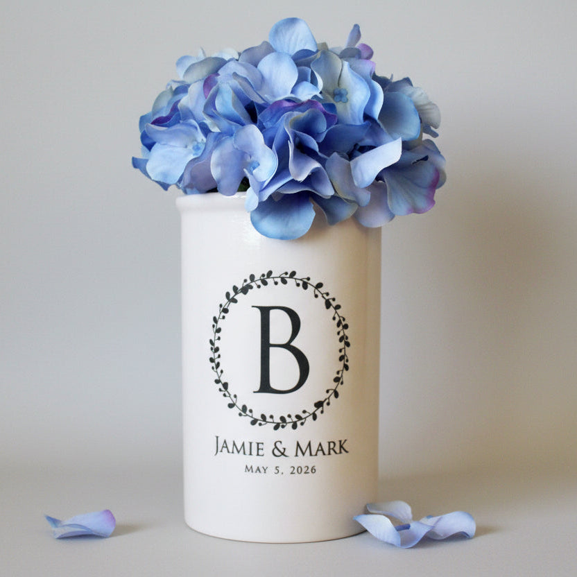 A white ceramic vase with a wreath design and a large initial in the center, personalized with the names 'Jamie and Mark' and a date 'May 5, 2026'.